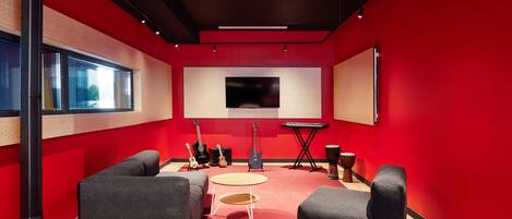 Un studio d’enregistrement aux murs rouges, équipé d’une console de mixage et d’instruments de musique.