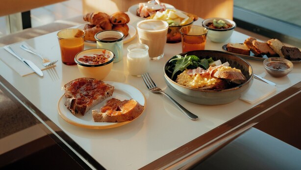 Una mesa de desayuno con diferentes alimentos y bebidas, una silla y vistas al exterior.
