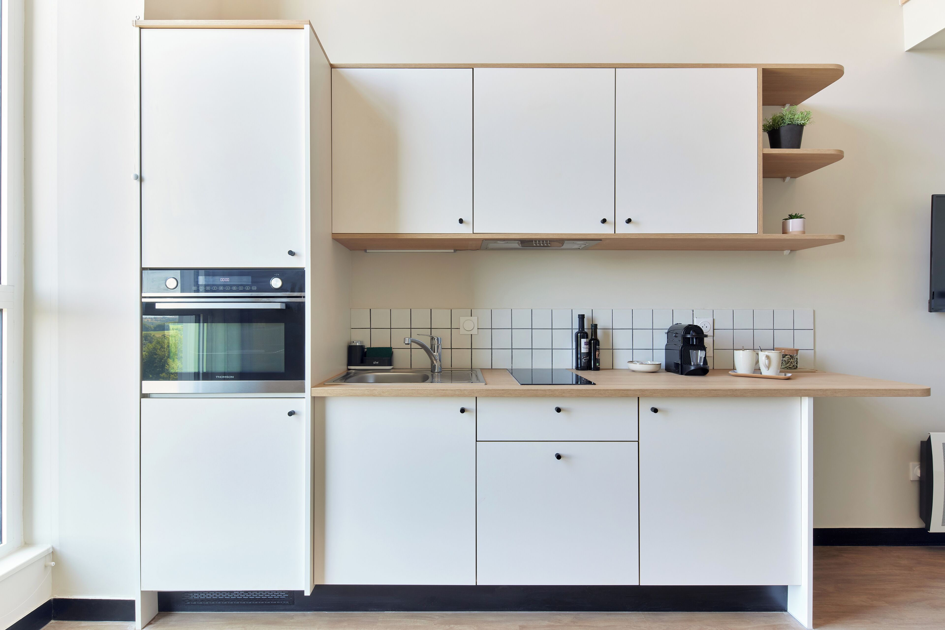 Uma cozinha moderna com armários brancos, forno embutido, micro-ondas, pia e cafeteira.