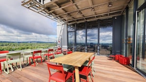 Un espacio de comedor al aire libre con mesa de madera y sillas rojas, ventanas amplias y vista al paisaje.