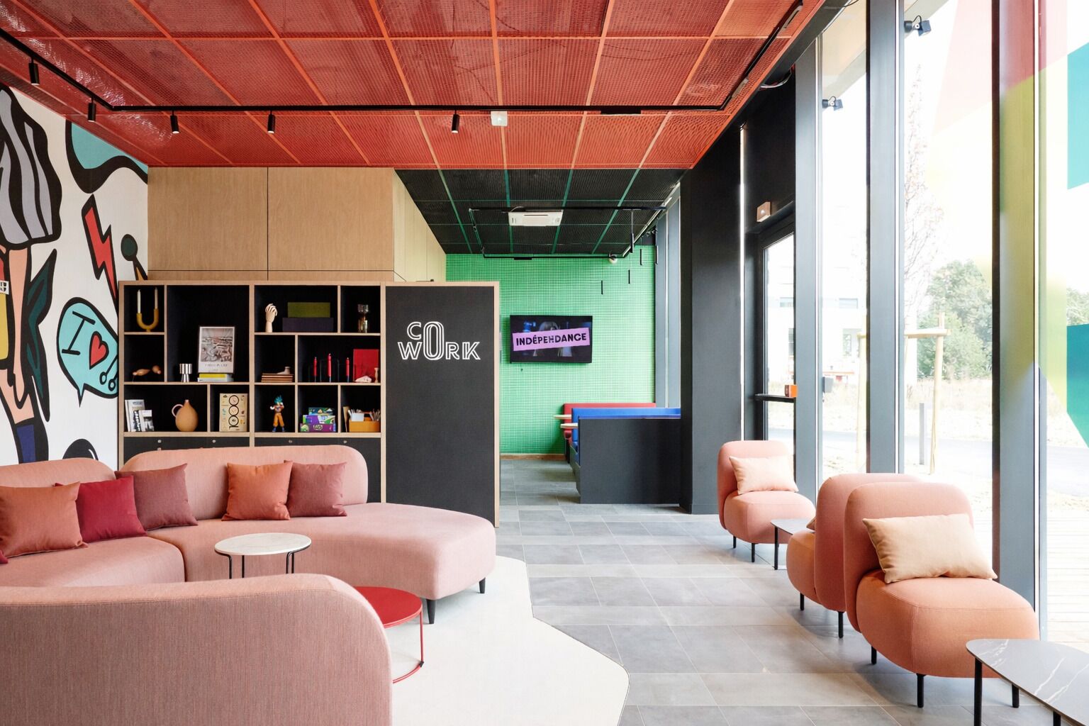 Un área de descanso moderna con sofás, una estantería y una pared verde con un televisor.