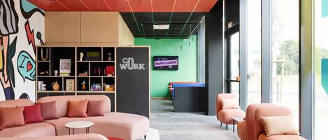 A modern lounge area with sofas, a bookshelf, and a green wall with a television.