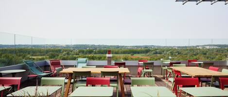 An outdoor seating area with tables and chairs, a view of the landscape, and a pergola structure.