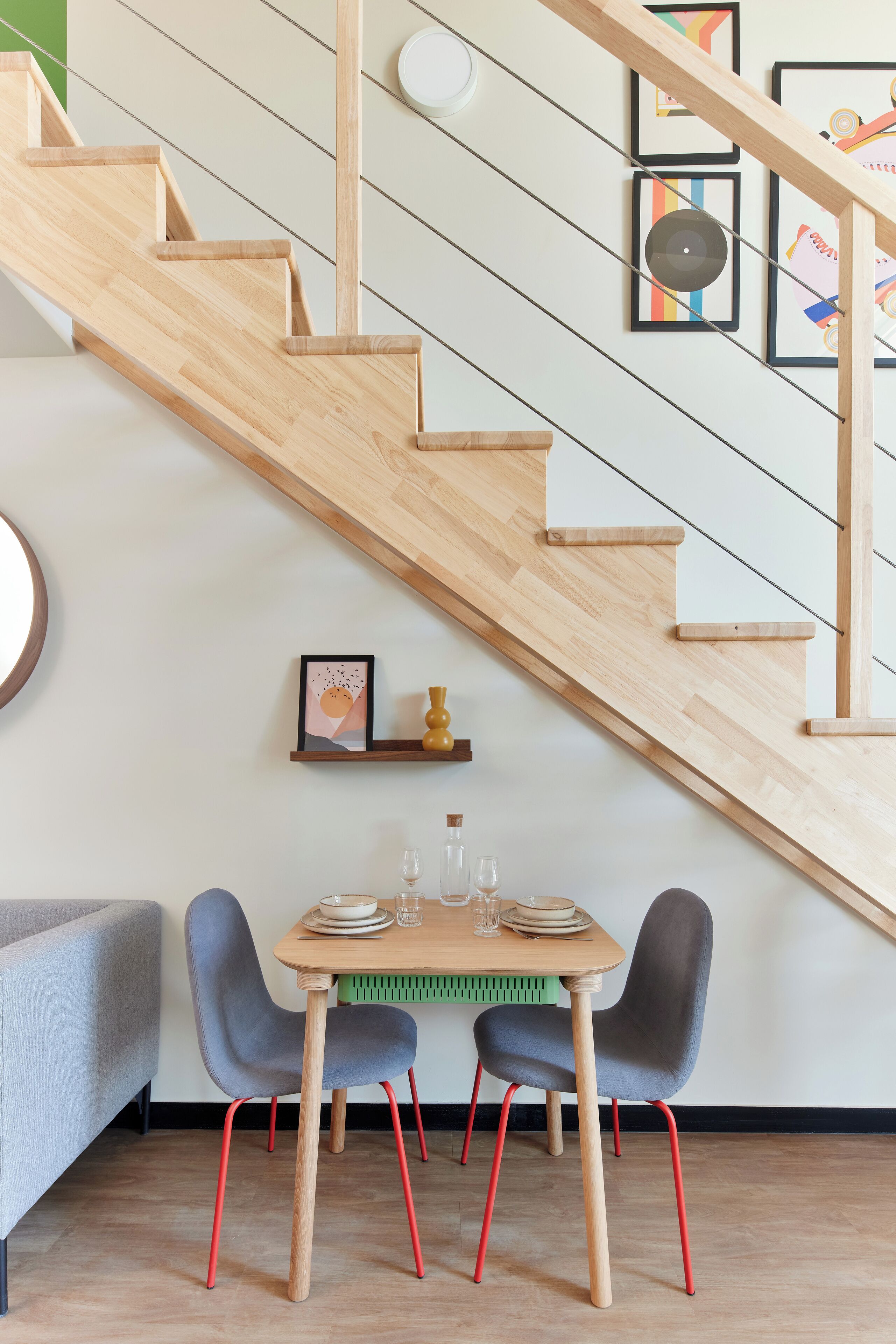 A staircase with wooden steps and a green wall. There is a table with chairs and a radiator below the stairs.