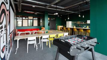 A modern indoor space with a foosball table, a long table with chairs, and a bar area.