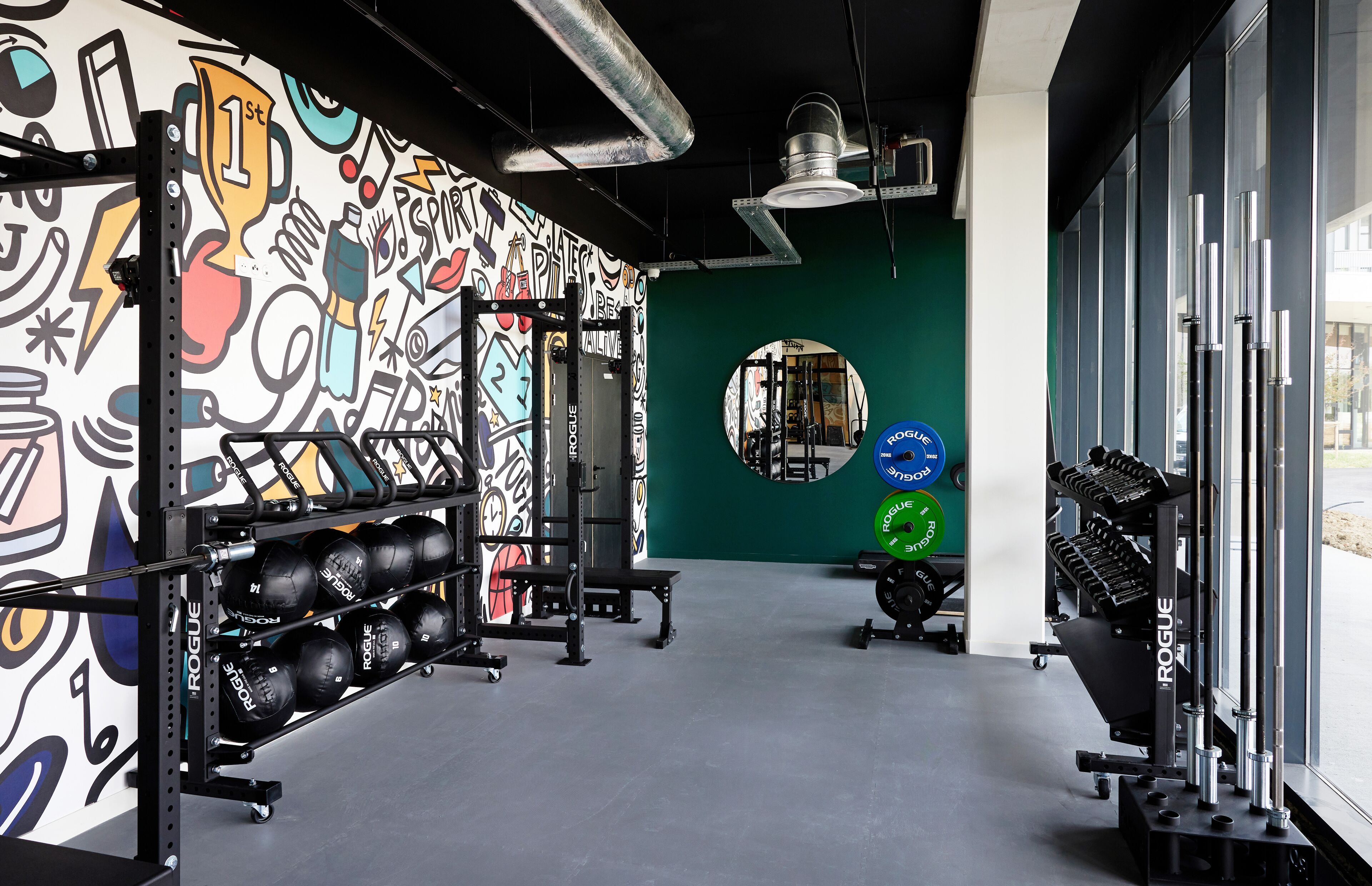 A gym with weightlifting equipment, a wall with colorful graffiti, and a large mirror.