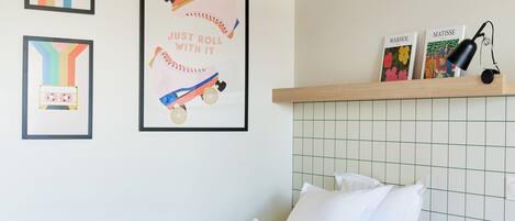 Un dormitorio ordenado con cama, almohadas, una estantería con libros y cuadros en la pared.