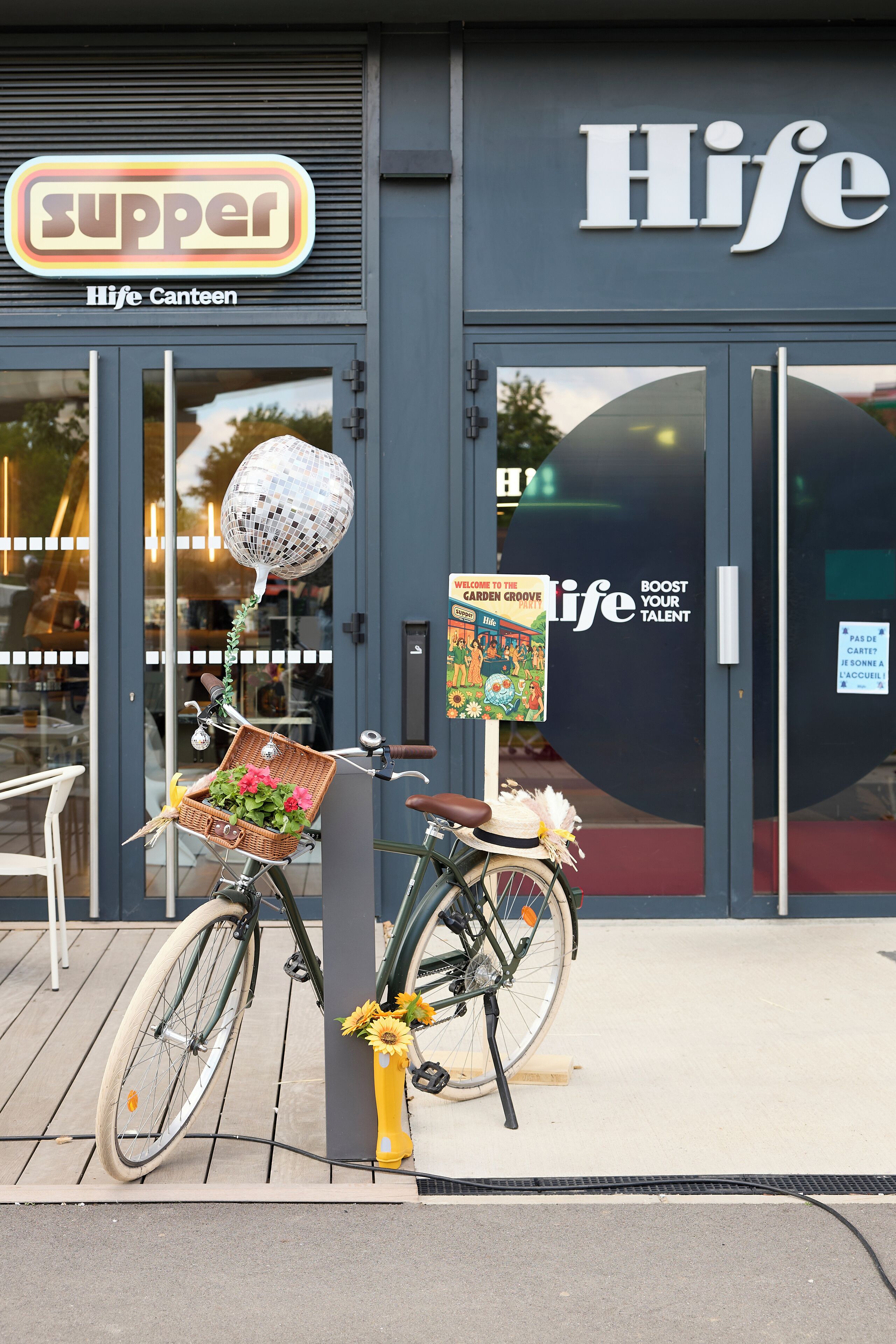 Una bicicleta con una canasta y un adorno de bola de discoteca estacionada frente a un edificio con un letrero que dice 'Hife Canteen'.