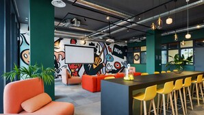 Un espacio de oficina moderno con una mesa grande, sillas coloridas, un mural y una pantalla de proyector.