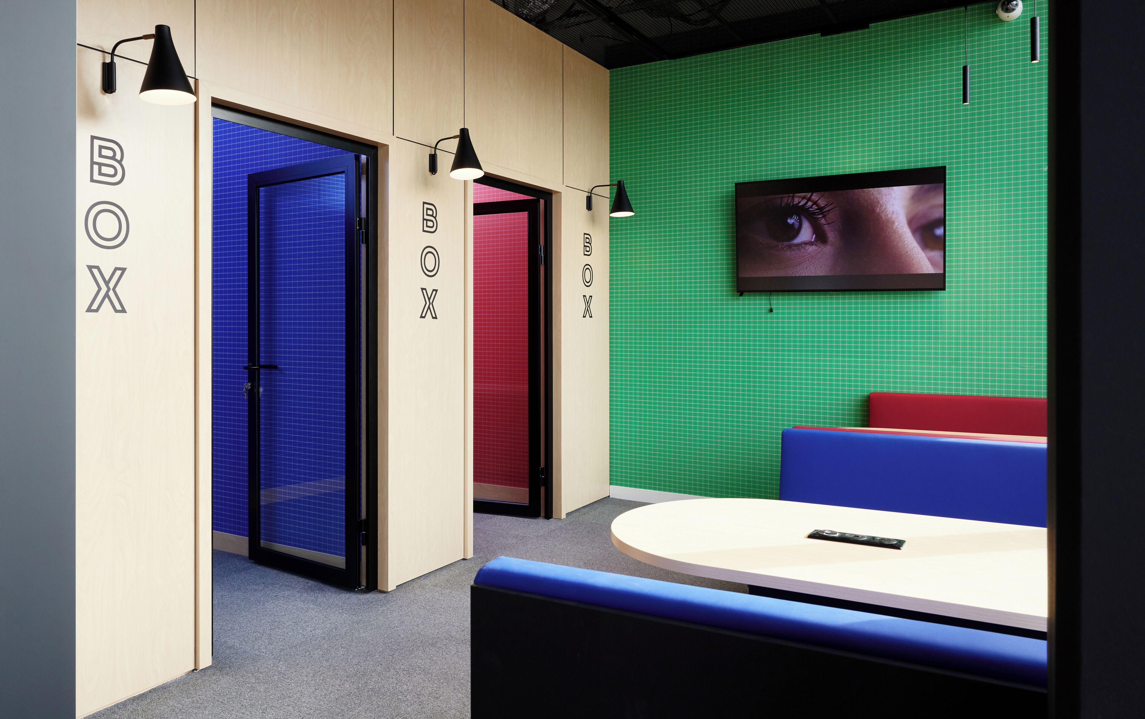 A modern office space with a green wall, a mounted screen displaying an image, and a seating area with a table.