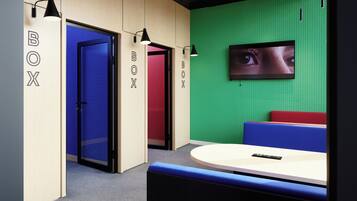 A modern office space with a green wall, a mounted screen displaying an image, and a seating area with a table.
