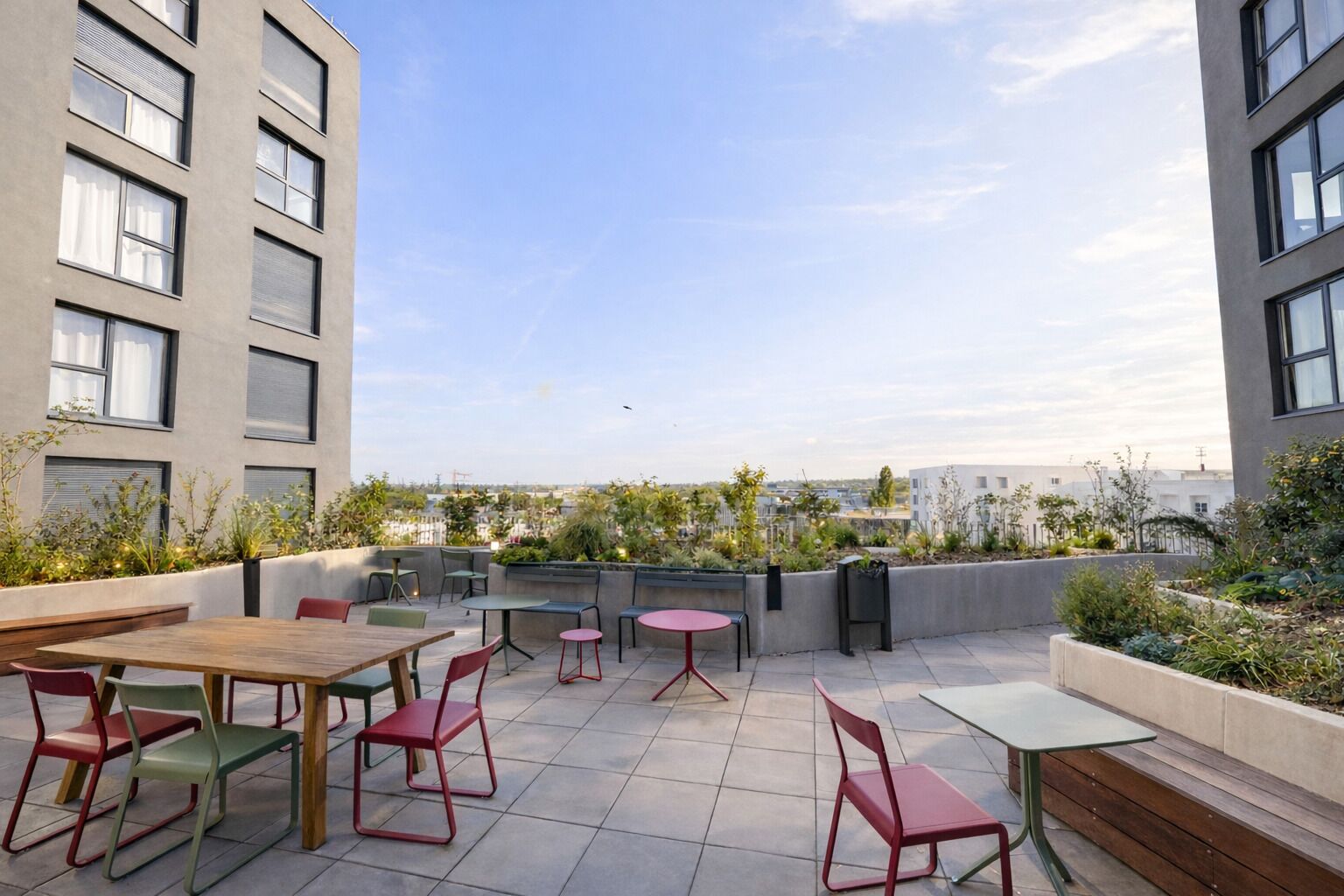 Une terrasse extérieure avec des tables et des chaises, entourée de verdure et offrant une vue sur le paysage urbain.