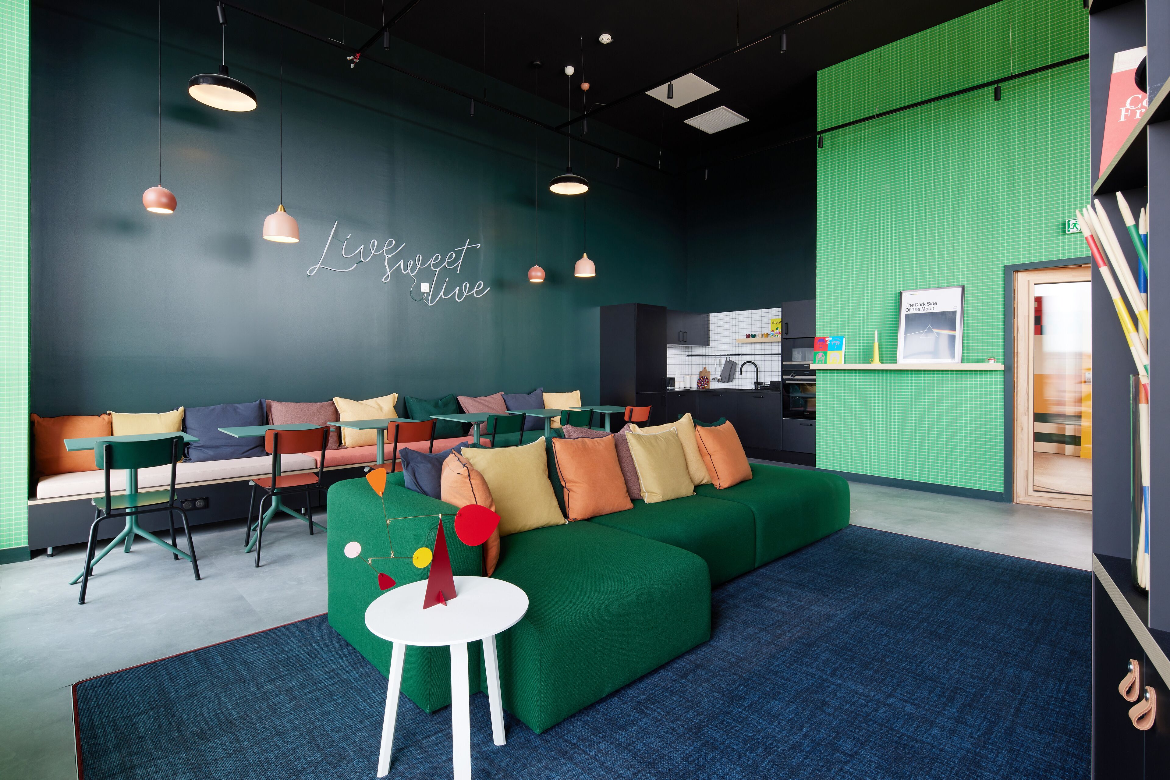 A modern lounge area with a green sofa, white tables, and colorful chairs.