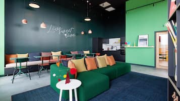 A modern lounge area with a green sofa, white tables, and colorful chairs.