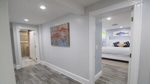 A hallway with a wooden floor leading to a bedroom with a bed and a wall-mounted fish painting.