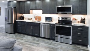 A modern kitchen with dark cabinets, stainless steel appliances, and a wood floor.