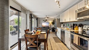 Uma cozinha moderna com eletrodomésticos de aço inoxidável, uma sala de jantar com mesa e cadeiras de madeira, e uma janela grande com vista para o quintal.