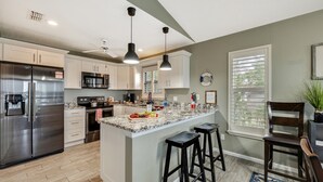 Cozinha moderna com eletrodomésticos de aço inoxidável, bancada de mármore e iluminação pendente.