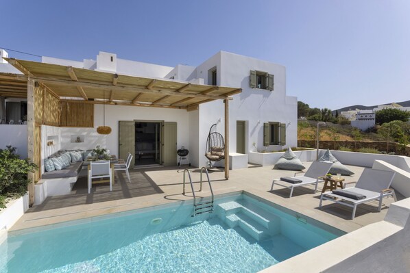 A rooftop pool area with a seating area, a pergola, and a view of the surrounding buildings.
