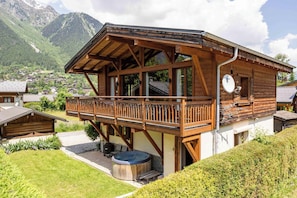 Una cabaña de madera con balcón, jacuzzi y vistas a un pueblo de montaña.