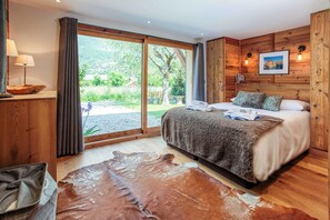 Un dormitorio con una cama grande, paredes de madera, un ventanal con cortinas y un tapete de cuero.