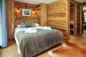 A wooden-paneled room with a bed, pillows, a blanket, and a cowhide rug.
