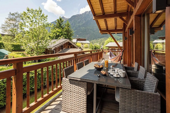 A wooden deck with a table set for breakfast, overlooking a mountainous landscape.