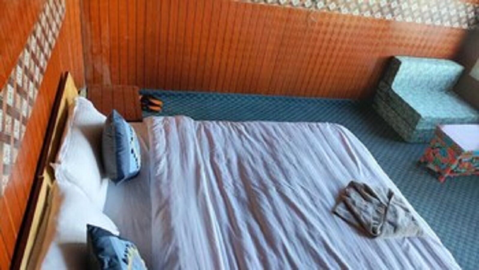Een enkel bed met kussens, een houten hoofdbord en een behang met patroon.