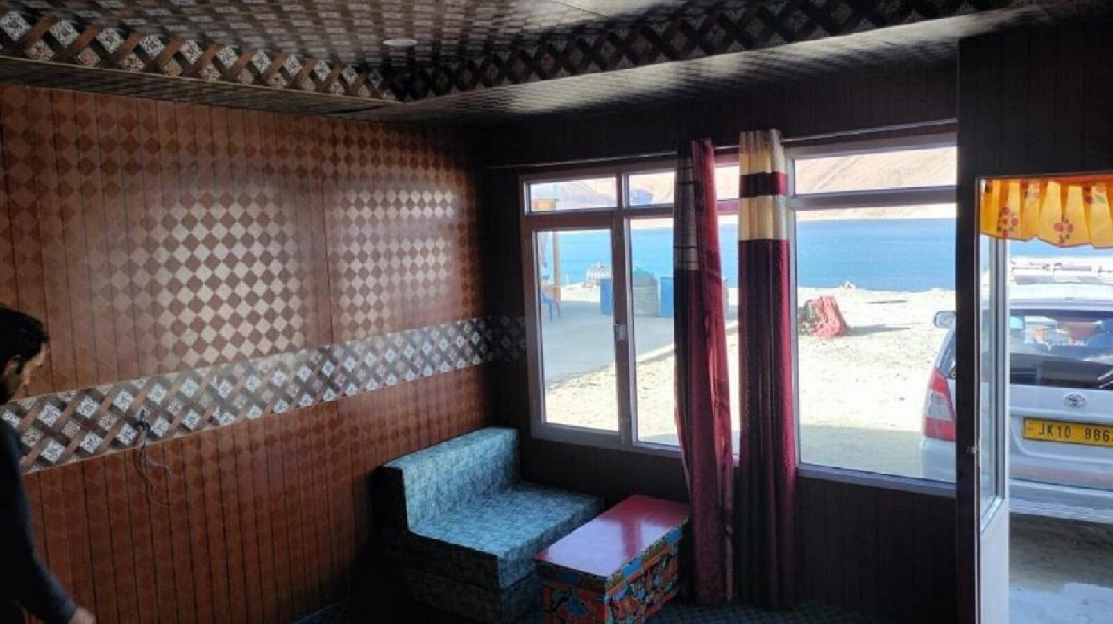 Una habitación con pared de diseño, un banco y una ventana con vista a la playa y coches estacionados.
