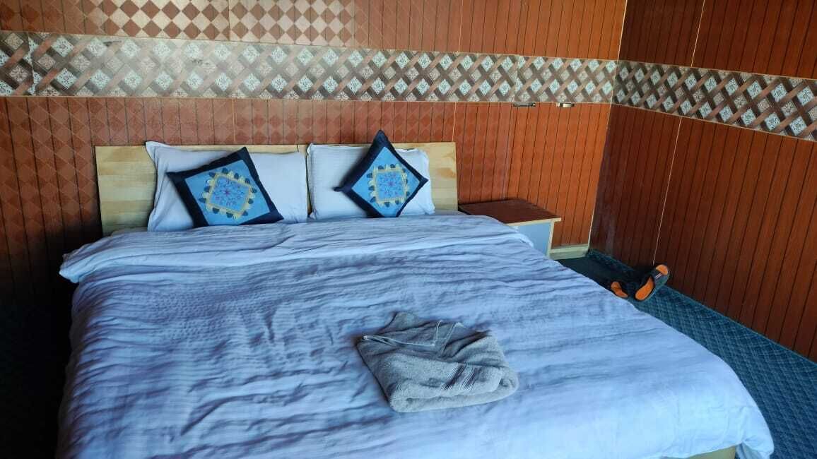 A neatly made bed with a blue and white bedspread, two decorative pillows, and a folded towel on the bed.