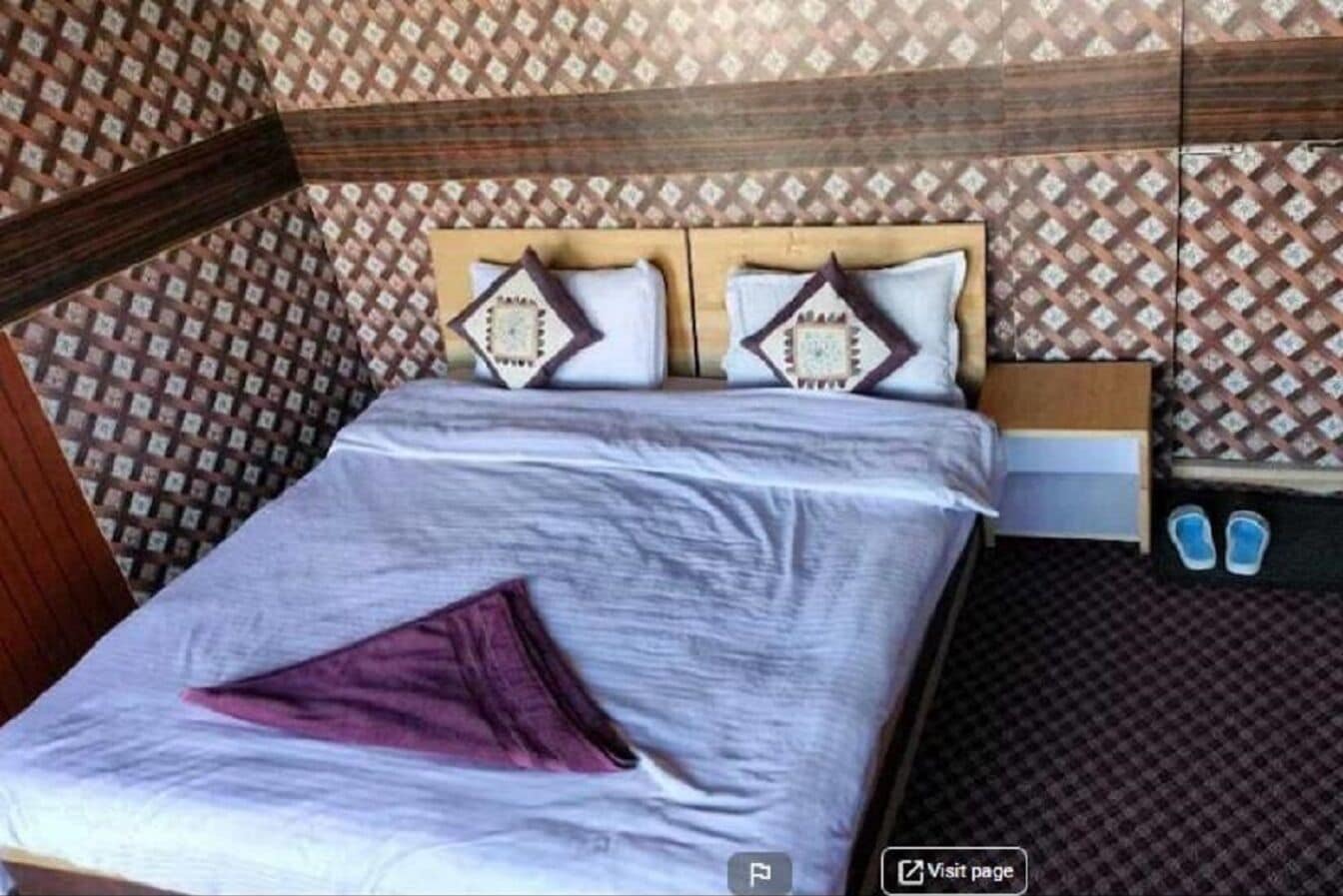 Uma cama com cabeceira de madeira, duas almofadas e um cobertor roxo.