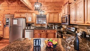 A kitchen with wooden cabinets, granite countertops, stainless steel appliances, and a hanging light fixture. - 3 Primary Suites, Amazing location, Hot Tub (Pigeon Forge)