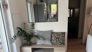 Una sala moderna con piso de madera, un tapete tejido grande, un banco empotrado con espacio de almacenamiento, una planta en maceta y un espejo amplio.