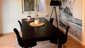 Un comedor con una mesa negra, una lámpara colgante de mimbre y un gran mural tropical en la pared.