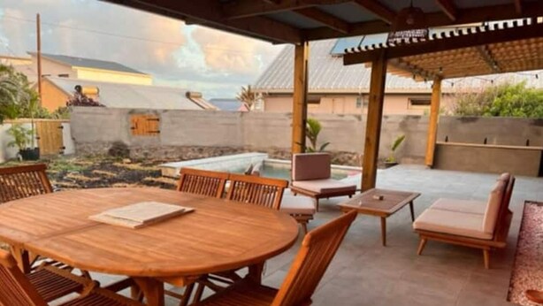 Un patio exterior con una mesa redonda de madera y sillas, un pequeño sofá y una silla de descanso.
