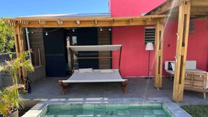 Un área junto a la piscina con terraza de madera, zona de estar techada y piscina.