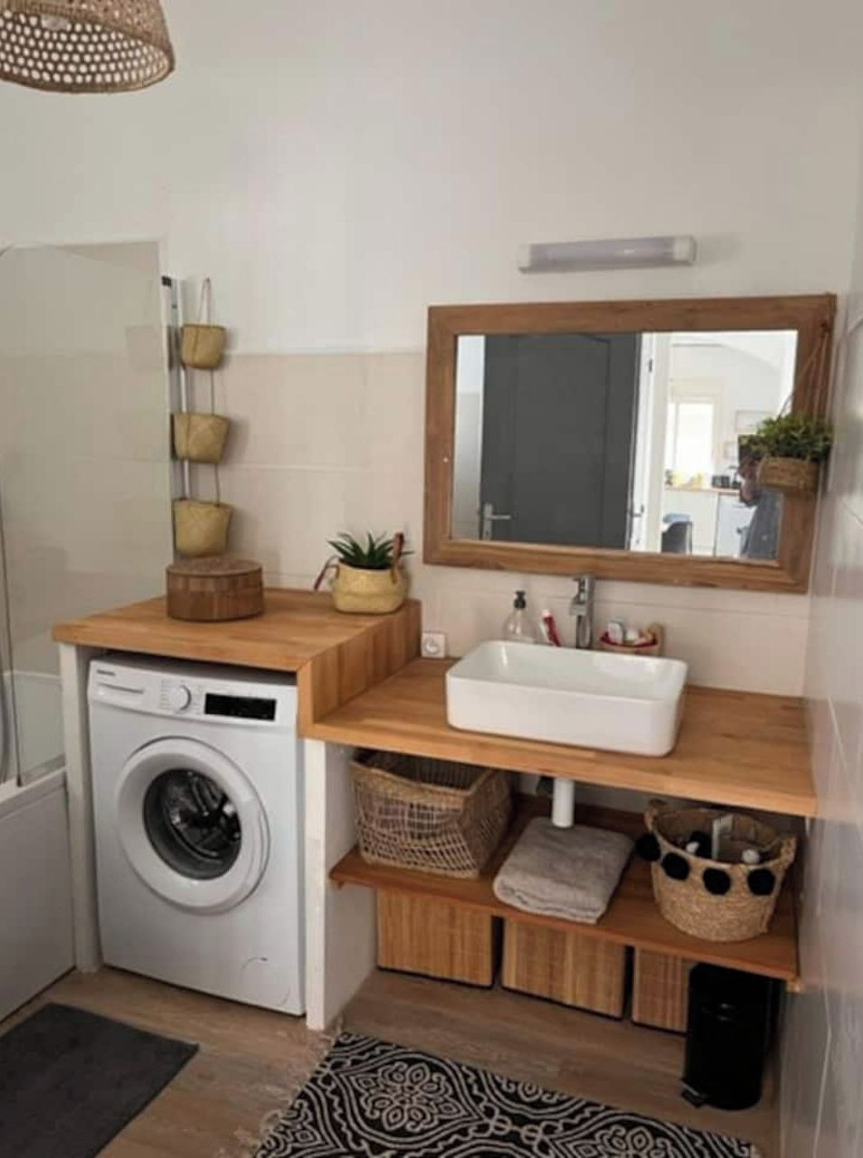 Un baño pequeño con lavadora, estantes de madera, un lavabo y un espejo.