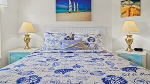 A bed with a blue and white floral bedspread, two bedside lamps, and a painting of sailboats on the wall.