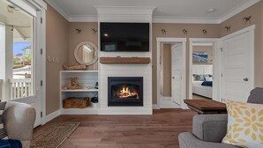 A living room with a fireplace, a television mounted above it, and a sofa with a patterned cushion. - Seabrook SeaDragon | Pet Friendly, Hot Tub, 3BR | Sleeps 9, Sunrise Pool (Pacific Beach)