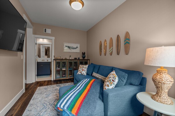 A living room with a blue sofa, a colorful throw blanket, a woven lamp, and surfboards on the wall.