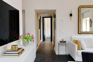 Un salon moderne avec un canapé blanc, une petite table d’appoint, un miroir et un couloir menant à une autre pièce.