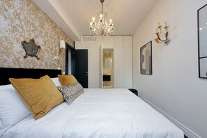 Une chambre d’hôtel avec un grand lit, un lustre, un miroir et une porte donnant sur une salle de bain.