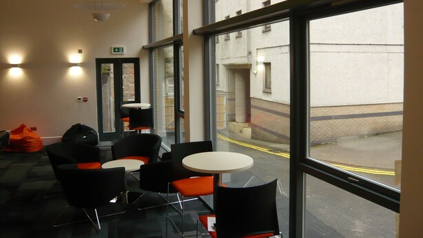 Un intérieur moderne avec de grandes fenêtres, des chaises noires et orange, et une table blanche.