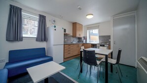 Une petite cuisine équipée avec un four à micro-ondes, une cuisinière et un évier. On y trouve un canapé bleu et une petite table à manger avec des chaises.