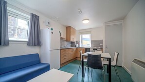 Une petite cuisine équipée comprenant un réfrigérateur, une cuisinière et un évier. On y trouve également un canapé bleu et une petite table à manger avec des chaises.