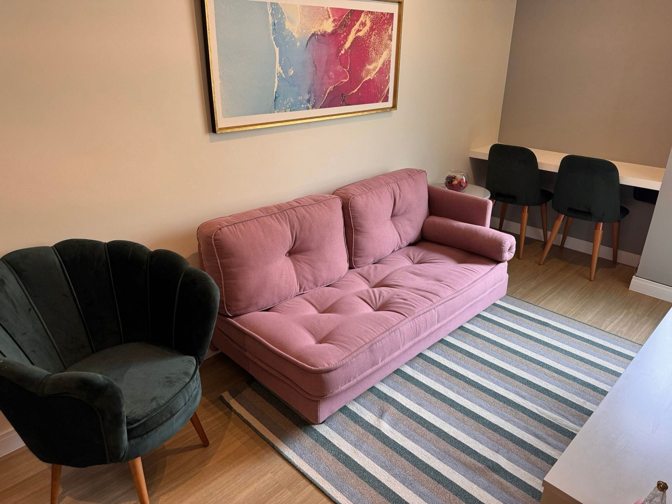A living room with a pink sofa, a dark armchair, and a striped rug.