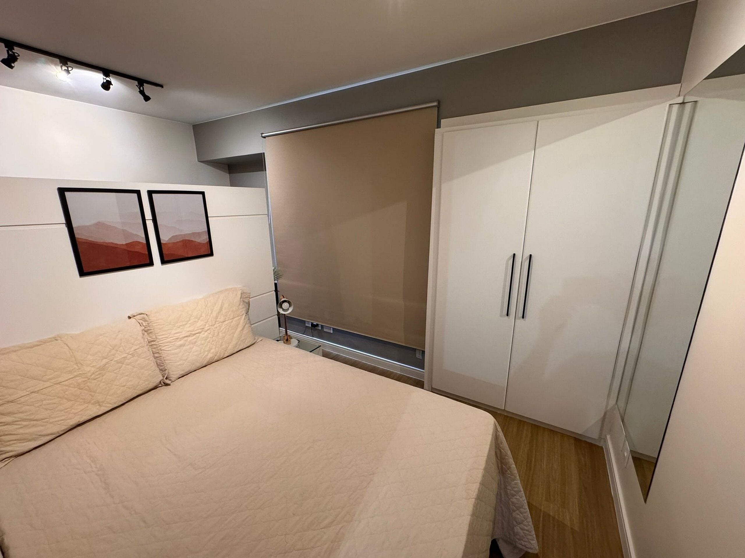 Quarto com uma cama, duas imagens penduradas na parede, um guarda-roupa e um candeeiro de teto.