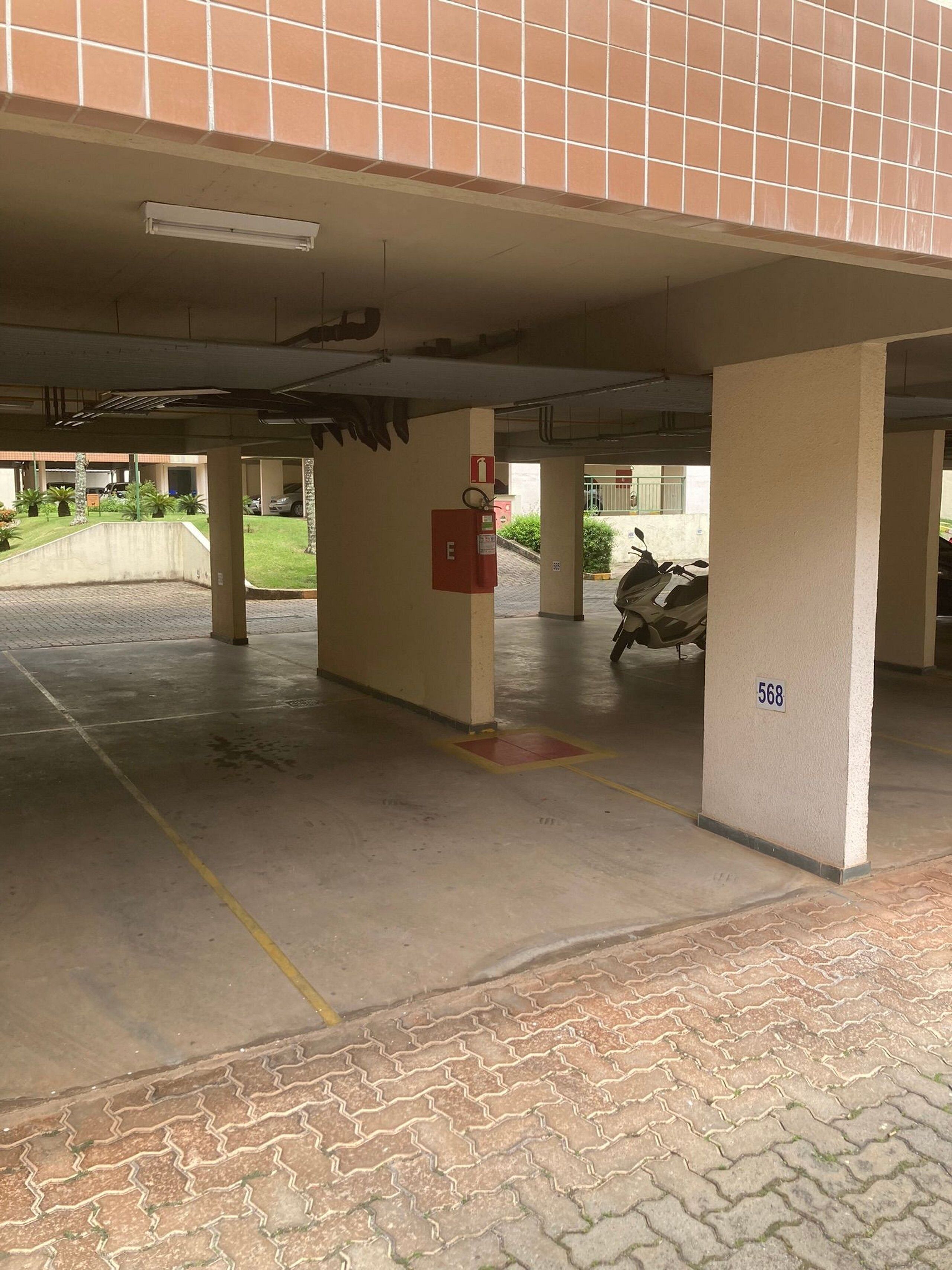A covered parking area with concrete pillars, a fire extinguisher, and a motorcycle.