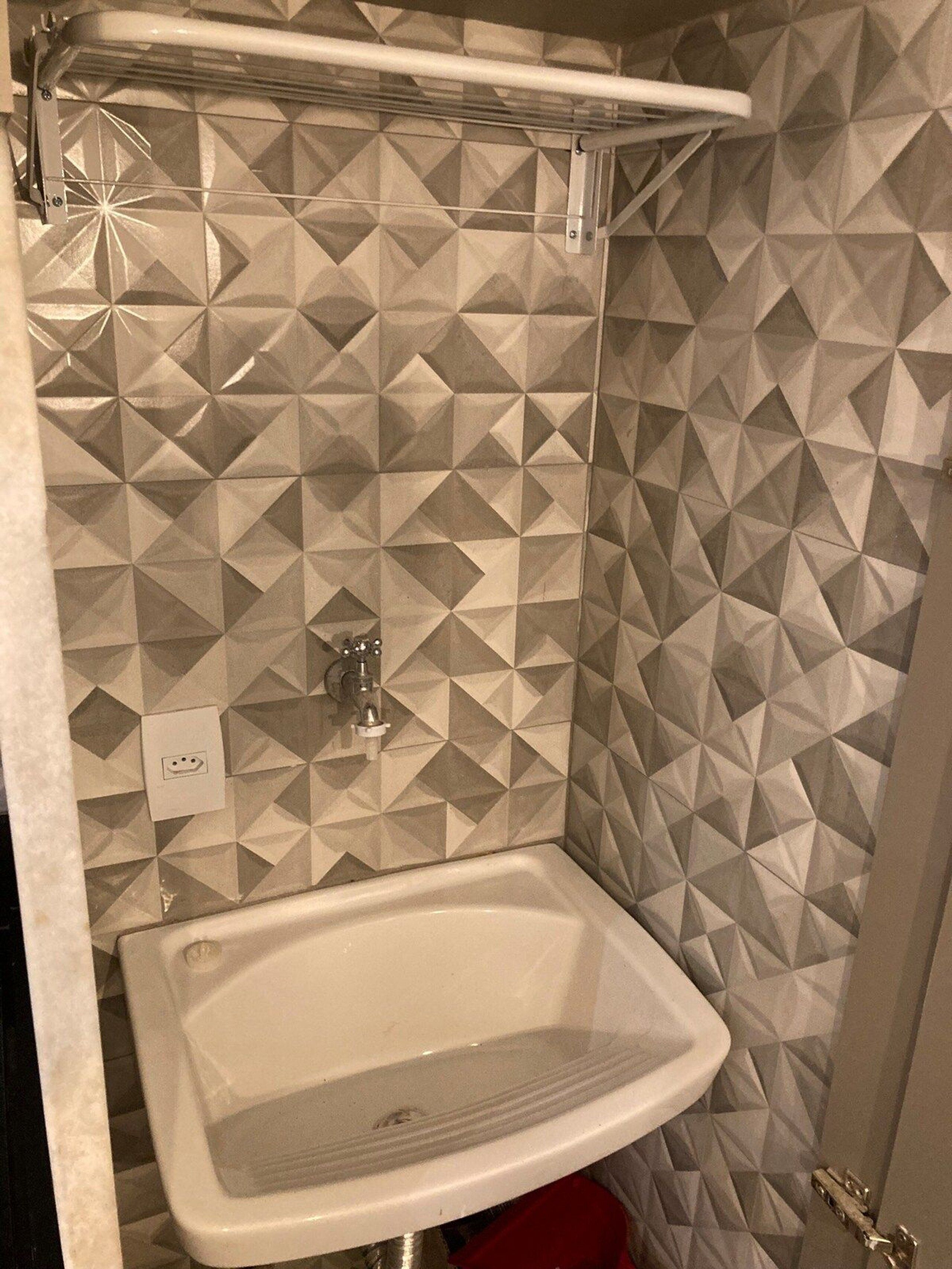 Un baño con pared de diseño geométrico, un lavamanos blanco y una zona de ducha.