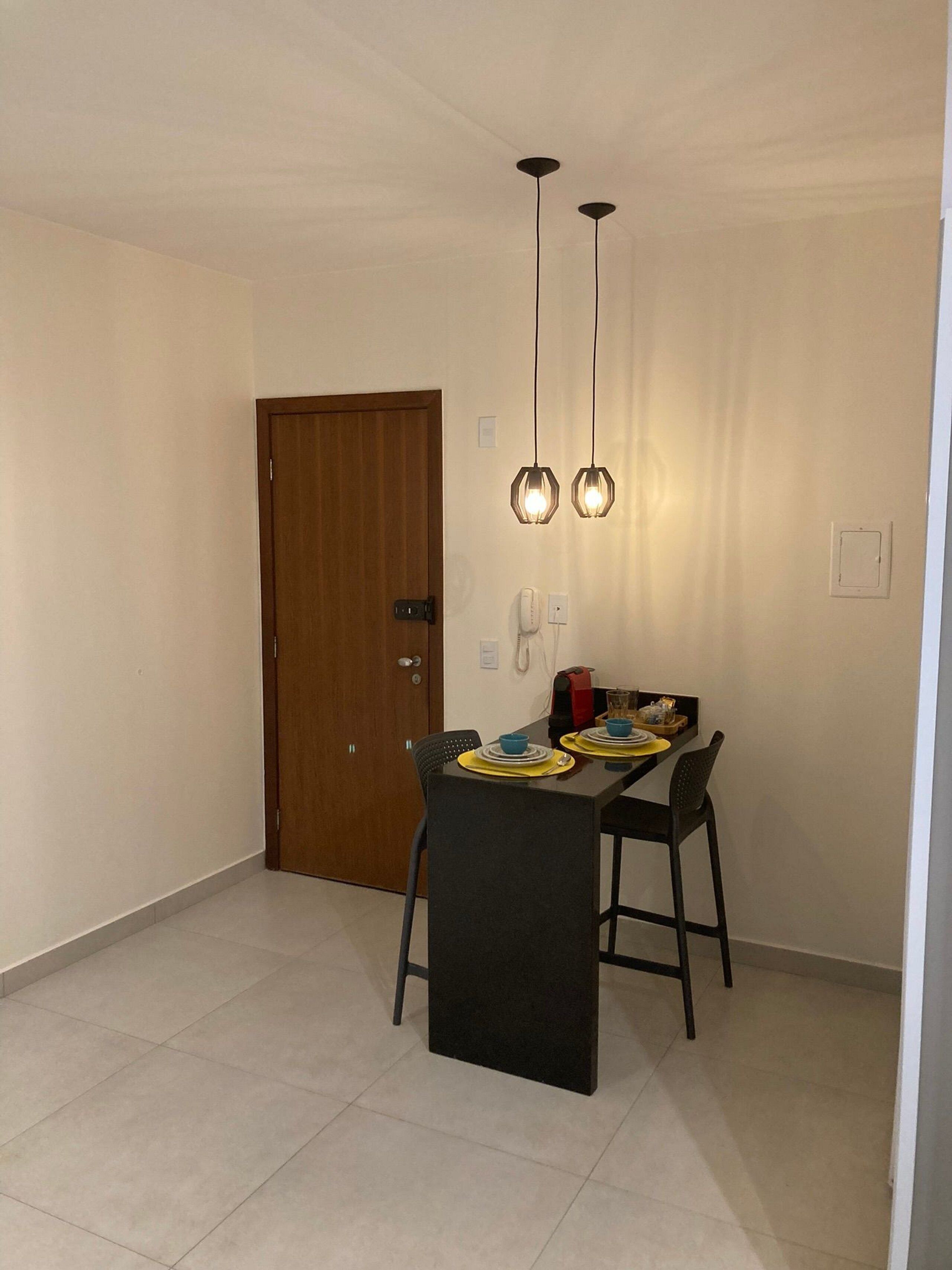 Zona pranzo con tavolo apparecchiato per due, una porta in legno e lampade a sospensione.